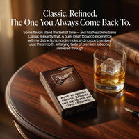 A dark brown pack of Gio Neo Demi Slims cigarettes sits on a polished wooden table next to a glass of whiskey with ice, with a book and pen nearby. White text at the top reads 'Classic.