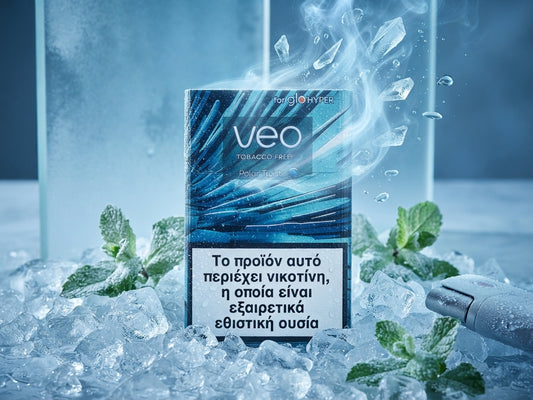 A pack of Veo Tobacco Products disposable cigarettes stands upright in a bed of ice with mint leaves and a vape device nearby. The packaging is blue and black with a large white health warning in Greek and the brand name 'veo' prominently displayed.