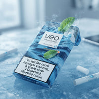 A pack of Veo Tobacco Free Arctic Coke disposable cigarettes in a blue icy pack design with mint leaves, shown on ice with two loose cigarettes and a blurred smartphone in the background.