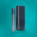 The image shows two components of the IQOS ILUMA i PRIME Kit against a turquoise background. On the left is a slim, silver-colored device with the IQOS logo, and on the right is a larger, black textured device.