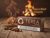 A box of Terea Bronze mellow tobacco blend for 100S Ilima, styled on a rustic wooden table with cinnamon sticks, star anise, and a bowl of loose tobacco with rising steam. The background features a warm, blurred fire, and text overlays read 'Mellow Tobacco Blend Warm Character'.