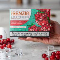 A hand holds a box of iSENZIA Zero Tobacco Red Berries Polar Crush nicotine tea sticks. The packaging features a vibrant red and green berry illustration, with scattered red berries and ice cubes on a light marble surface in the foreground.
