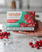 A hand holds a box of iSENZIA Zero Tobacco Red Berries Polar Crush nicotine tea sticks. The packaging features a vibrant red and green berry illustration, with scattered red berries and ice cubes on a light marble surface in the foreground.